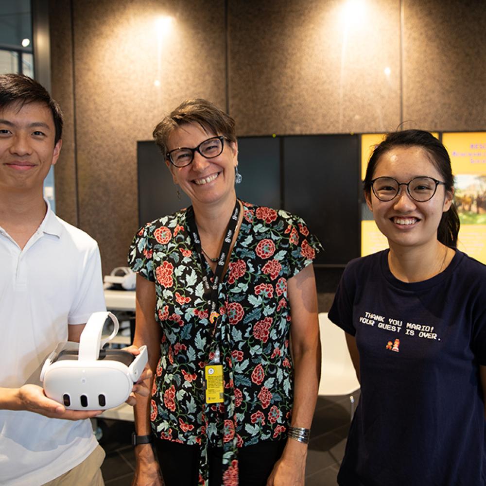 Three people standing holding a VR head set